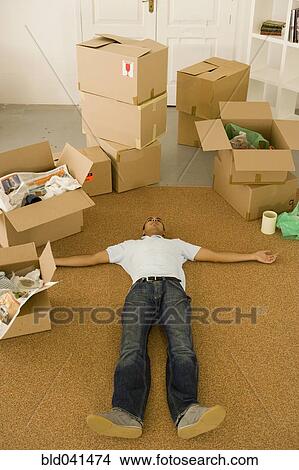 Picture - Man laying on floor next to moving boxes. Fotosearch