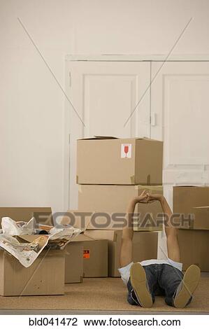 Stock Image - Man laying on floor next to moving boxes. Fotosearch