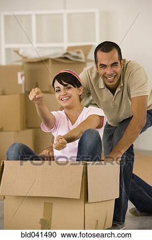 Stock Image - Man pushing wife in moving box. Fotosearch