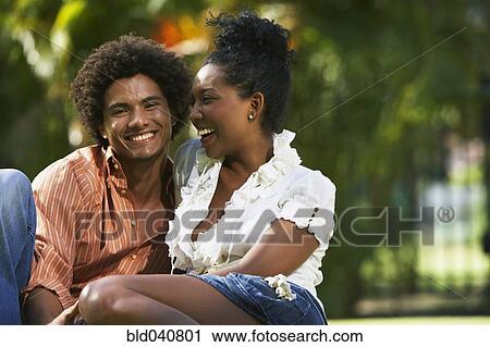 Stock Image - South American couple sitting in park. Fotosearch