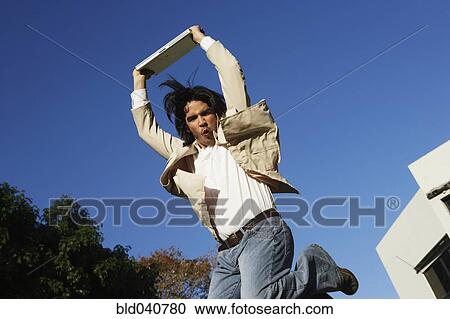 Stock Image - South American man jumping with laptop. Fotosearch