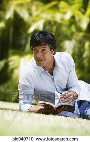Stock Image - South American man reading in grass. Fotosearch