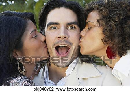 Stock Image - Two women kissing man on cheek. Fotosearch
