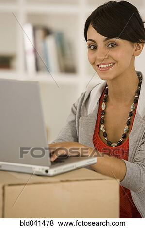 Stock Photo - Woman using laptop on moving box. Fotosearch