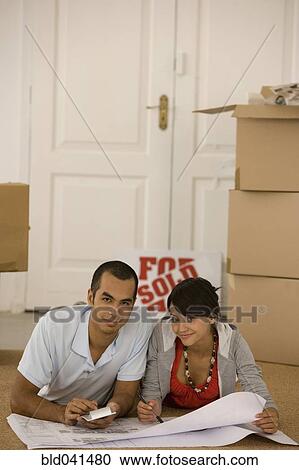 Stock Image - Young couple looking at blueprints in new house. Fotosearch