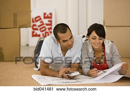 Stock Image - Young couple looking at blueprints in new house. Fotosearch