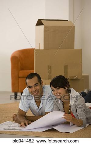 Stock Image - Young couple looking at blueprints in new house. Fotosearch