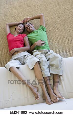Stock Image - Young couple on floor with feet on sofa. Fotosearch