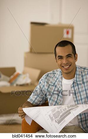 Picture - Young man looking at blueprints in new house. Fotosearch