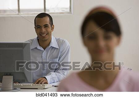Young man sitting at desk View Large Photo Image Stock Image - Young man sitting at desk. Fotosearch
