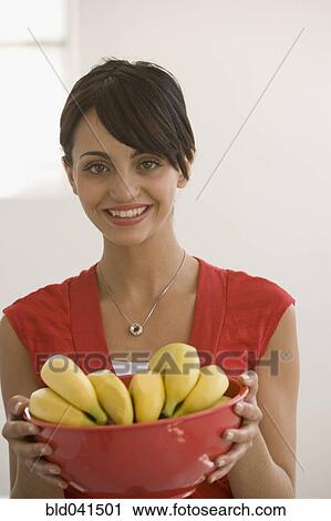 Stock Image - Young woman holding bowl of bananas. Fotosearch