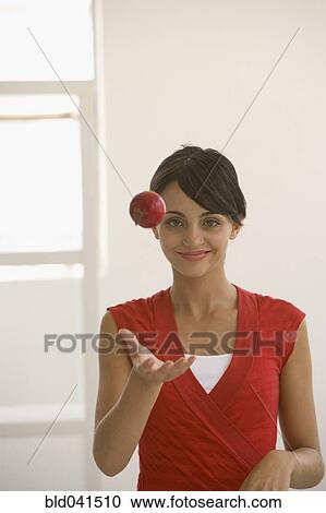 Stock Image - Young woman throwing apple in air. Fotosearch