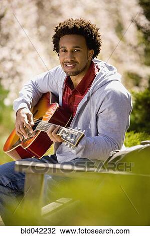 Stock Image - African American man playing acoustic guitar. Fotosearch