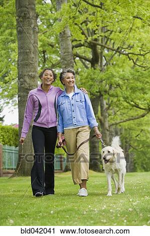 Stock Image - African American mother and adult daughter walking dog. Fotosearch