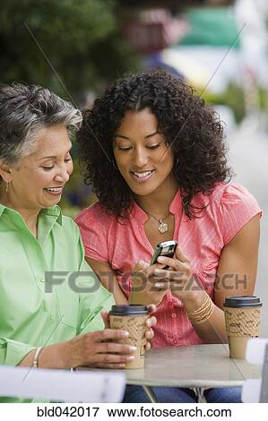 Stock Photo - African American mother and adult daughter looking at cell phone. Fotosearch