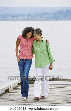 Stock Photo - African American mother and adult daughter walking on pier. Fotosearch