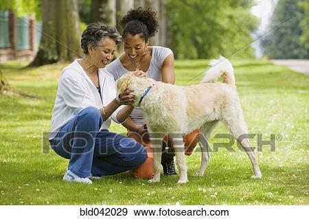 Stock Photo - African American mother and adult daughter petting dog. Fotosearch