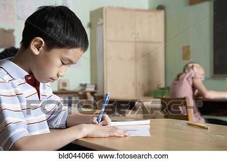 Stock Photograph - Asian boy writing in classroom. Fotosearch
