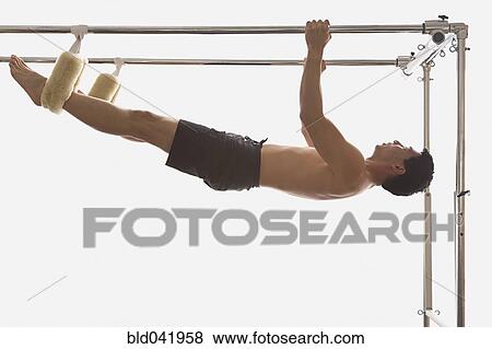 Stock Photo - Asian man hanging on exercise equipment. Fotosearch