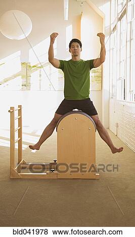 Stock Photo - Asian man sitting in exercise equipment. Fotosearch