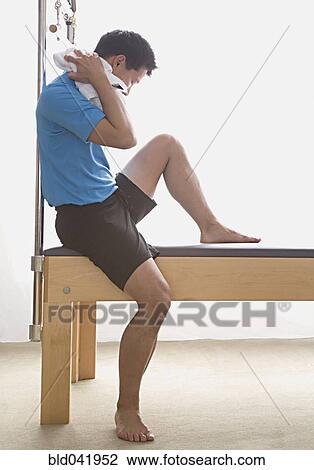 Stock Image - Asian man sitting on exercise equipment. Fotosearch