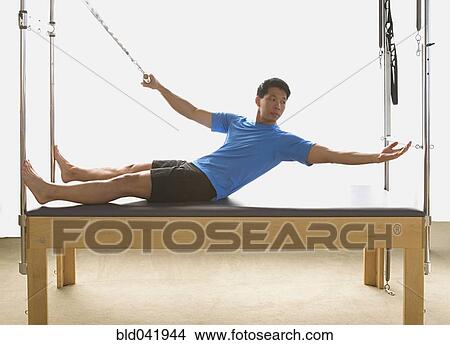 Picture - Asian man stretching on exercise equipment. Fotosearch