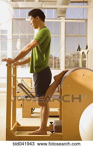 Stock Image - Asian man stretching on exercise equipment. Fotosearch