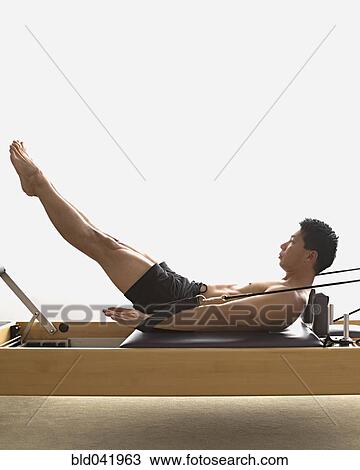 Stock Image - Asian man stretching on exercise equipment. Fotosearch