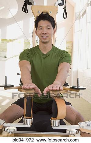 Stock Image - Asian man stretching on exercise equipment. Fotosearch