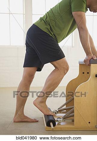 Stock Image - Asian man stretching on exercise equipment. Fotosearch