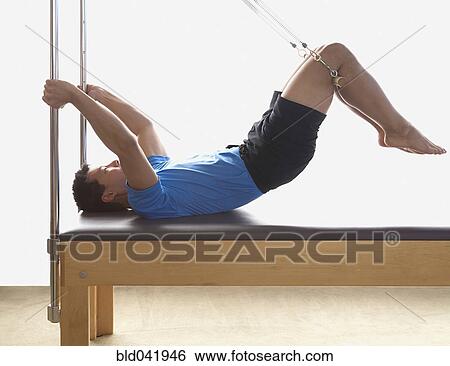 Stock Photograph - Asian man stretching on exercise equipment. Fotosearch