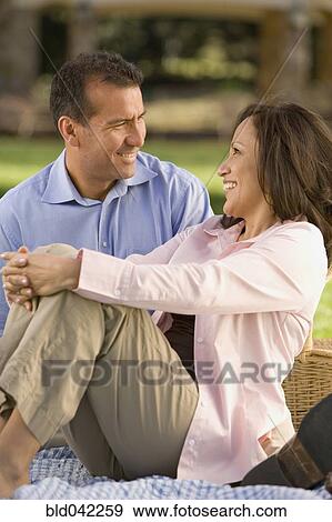 Stock Photo - Hispanic couple sitting on picnic blanket. Fotosearch