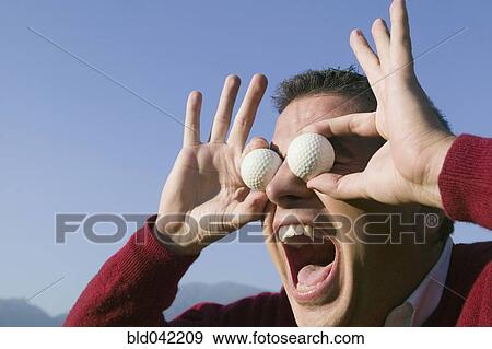 Stock Photo - Hispanic man holding golf balls over eyes. Fotosearch