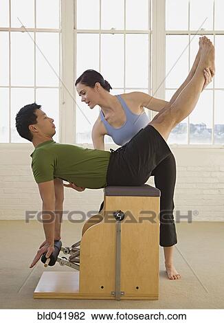 Stock Image - Instructor helping man in exercise studio. Fotosearch
