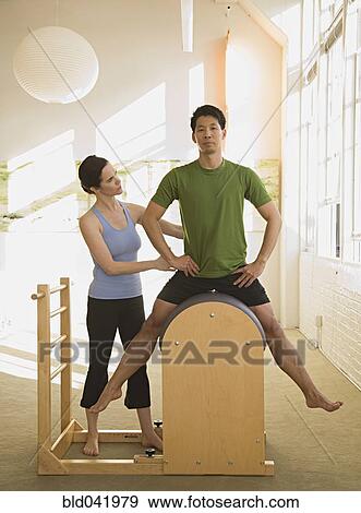 Stock Photo - Instructor helping man in exercise studio. Fotosearch
