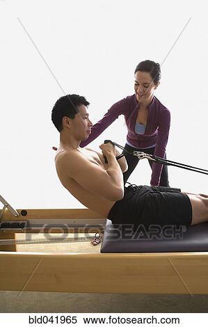 Stock Photography - Instructor helping man on exercise equipment. Fotosearch