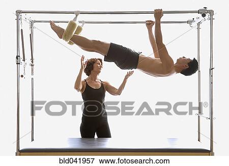 Stock Photo - Instructor spotting man on exercise equipment. Fotosearch