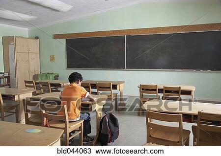 Stock Image - Mixed Race boy in empty classroom. Fotosearch
