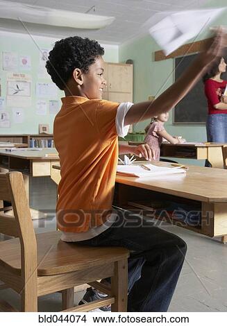 Picture - Mixed Race boy throwing paper airplane in class. Fotosearch