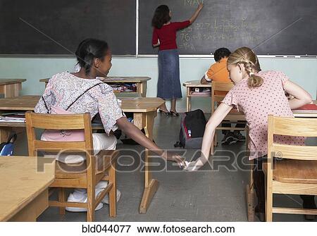 Stock Photo - Multi-ethnic girls passing note in class. Fotosearch