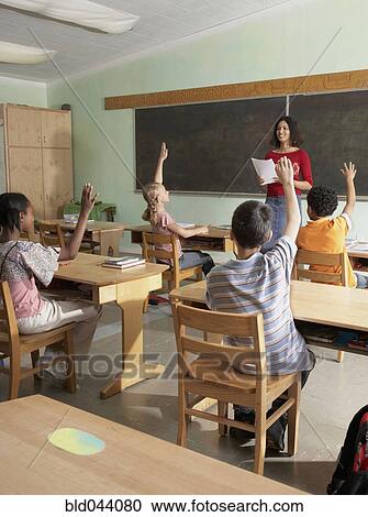 Stock Image - Multi-ethnic students raising hands in class. Fotosearch