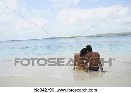 Stock Image - South American couple sitting on beach. Fotosearch