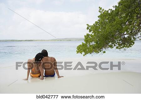 Stock Photo - South American couple sitting on beach. Fotosearch