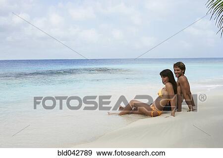 Stock Photo - South American couple sitting on beach. Fotosearch