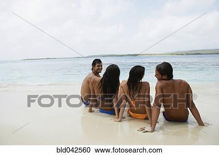Stock Image - South American couples sitting on beach. Fotosearch