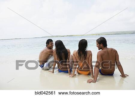 Stock Image - South American couples sitting on beach. Fotosearch