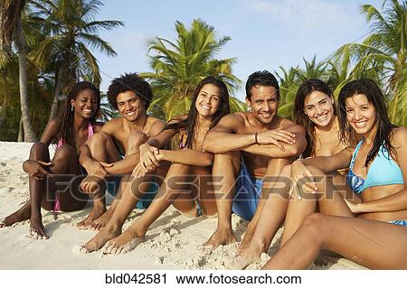 Stock Image - South American friends sitting on beach. Fotosearch