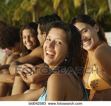 Stock Image - South American friends sitting on beach. Fotosearch