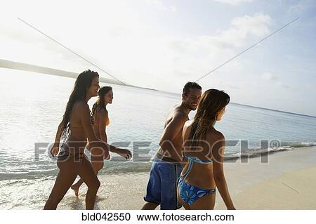 Stock Image - South American friends walking on beach. Fotosearch