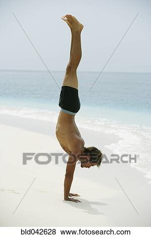 Stock Photo - South American man doing handstand at beach. Fotosearch